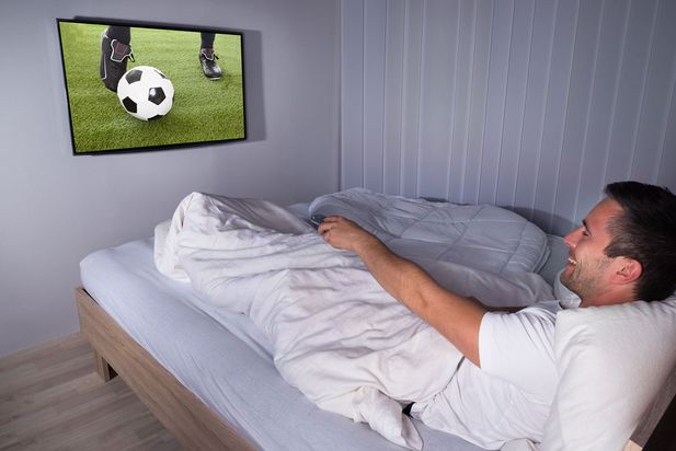 A man watching a football game in bed
